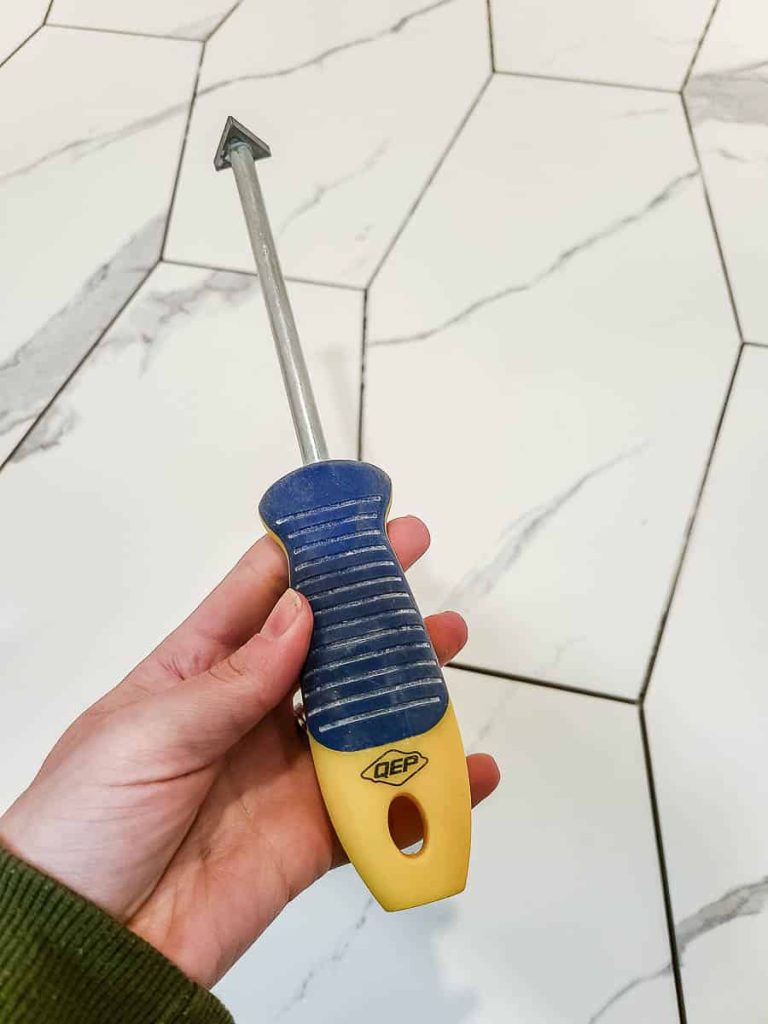 Tile scraper removing excess adhesive from ungrouted tiles.