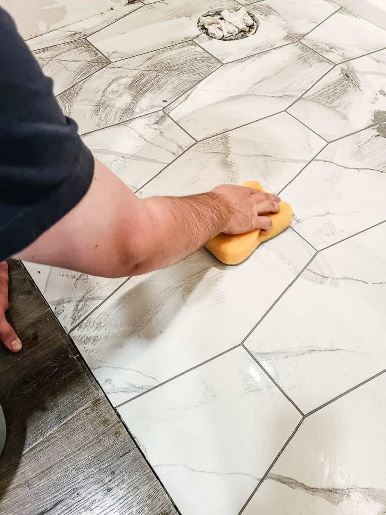 Gently pressing sponge along grout lines to clean newly tiled surface.