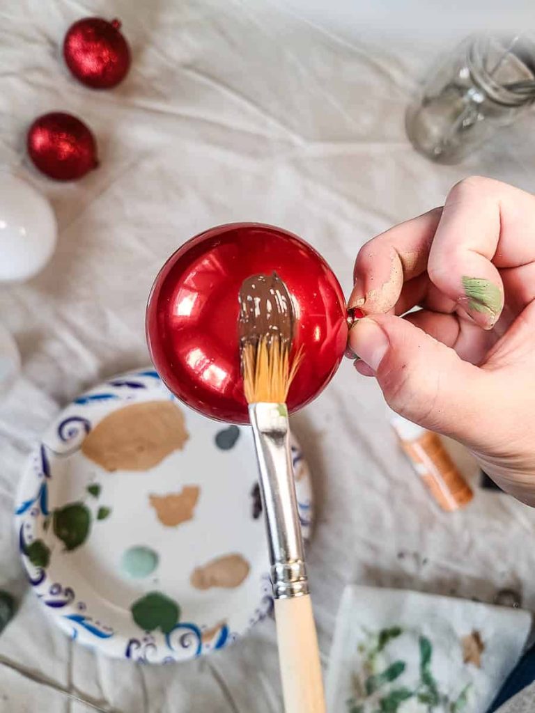 A woman is painting a Christmas ornament while holding it.