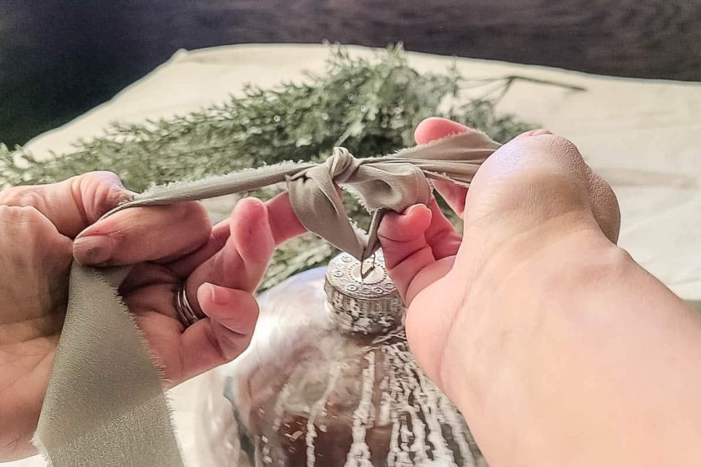 A person is adding a ribbon to the top of the ornament.