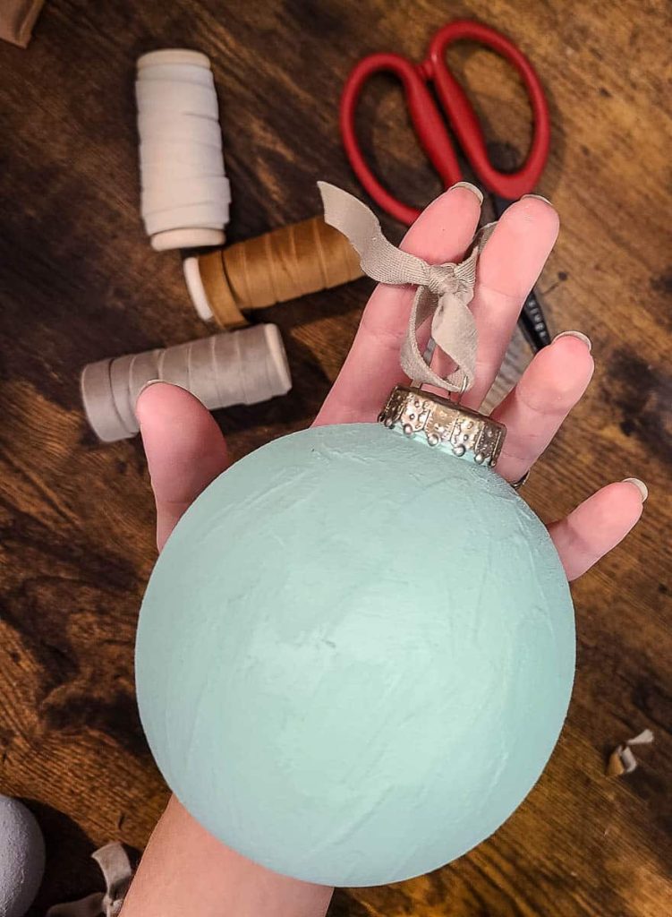 A person is holding finished textured ornaments with ribbon on top.