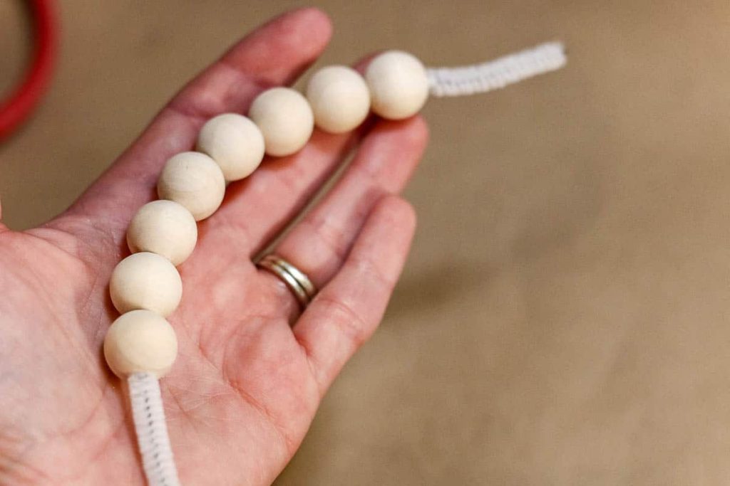 a person holding a  String wood beads onto the pipe cleaner.