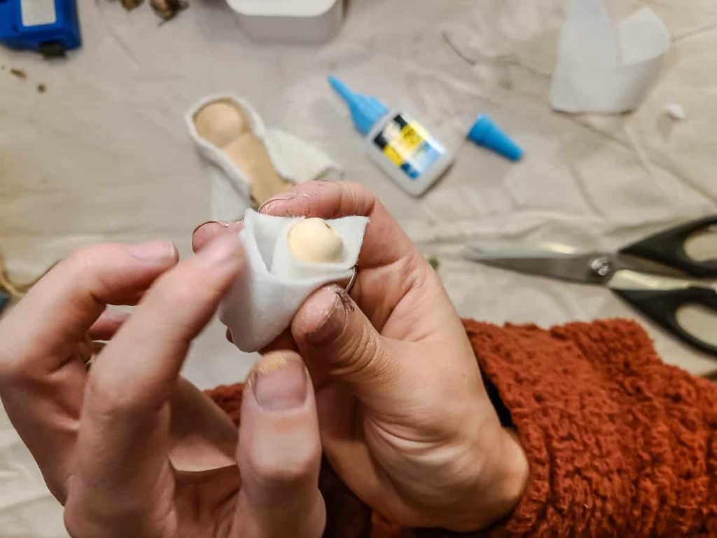 A person is wrapping a scrap of cloth into a wooden bead for use in the baby Jesus nativity scene.