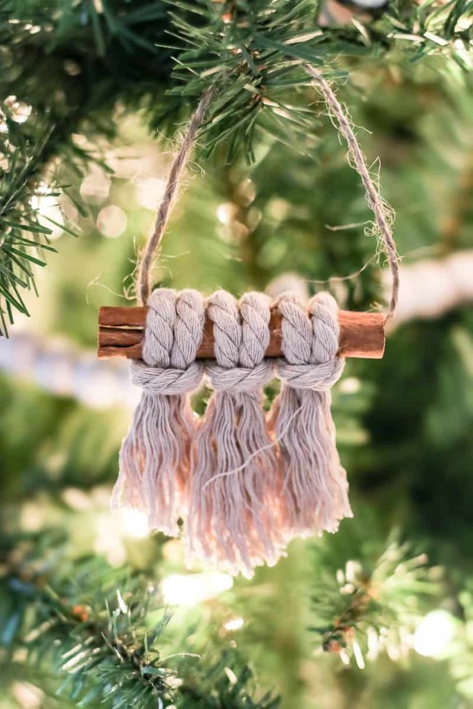 Two macrame Christmas ornaments, finished in a boho-style cinnamon stick design, decorate the christmas tree.