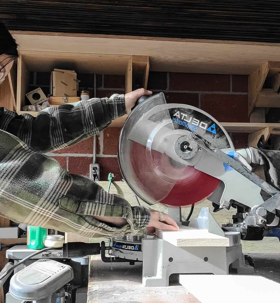 A man is cutting a wood down size with a miter saw.
