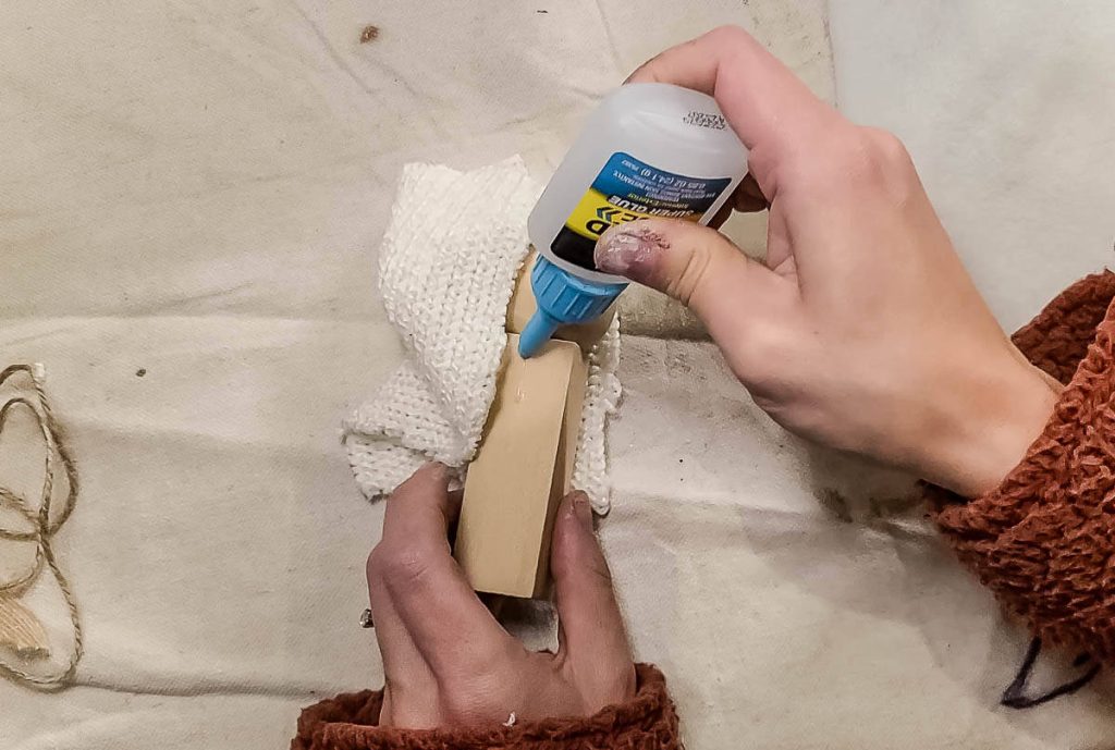 A person is gluing the glue to a piece of wood that has a bit of sweater glued onto it for Mary.