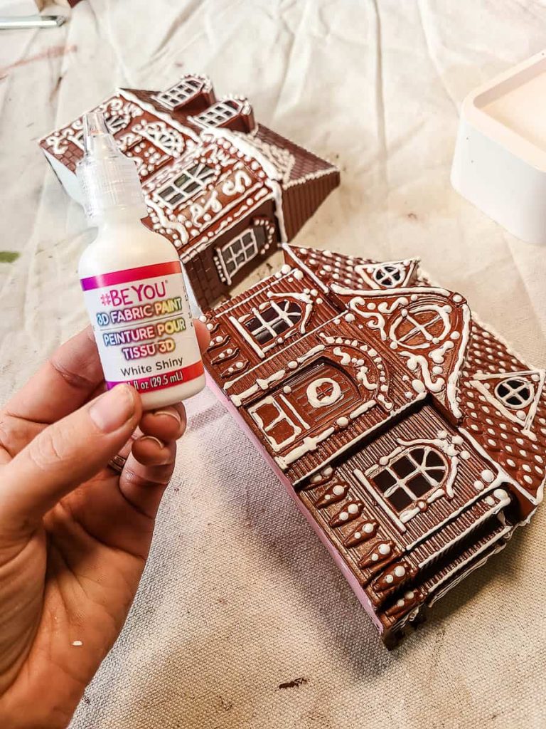 Finished gingerbread house adorned with white puffy paint, creating a snowy and textured masterpiece for festive holiday decor.