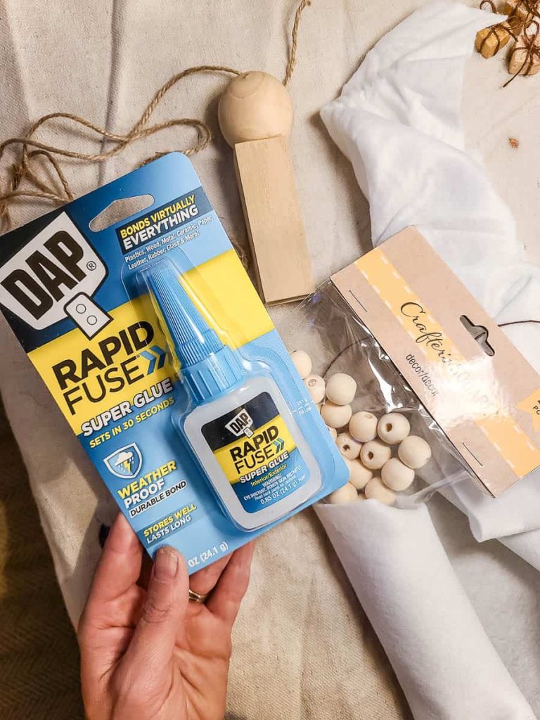 A person holds a bottle of super glue and some wooden beads to use a DIY Wood Nativity Scene.