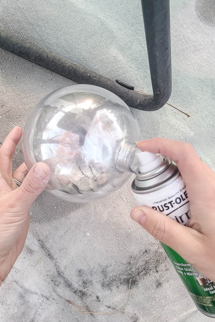 The person is coating the inside of the ornament with a layer of mirror spray paint.