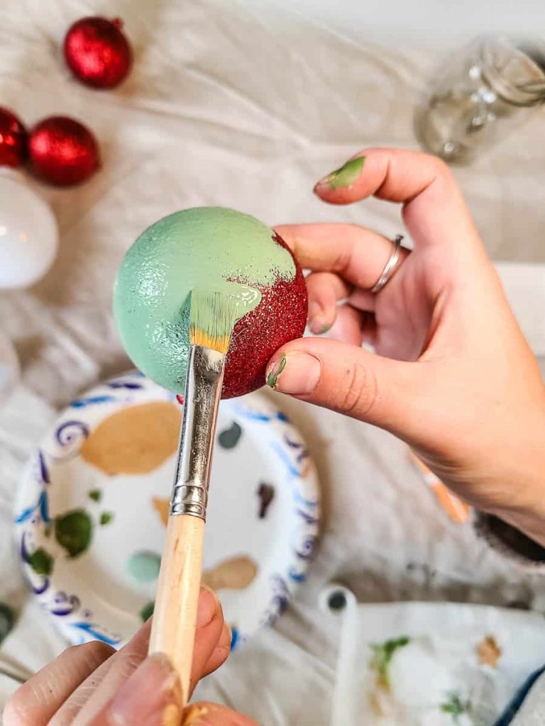 A person is holding an ornament, painting it green.