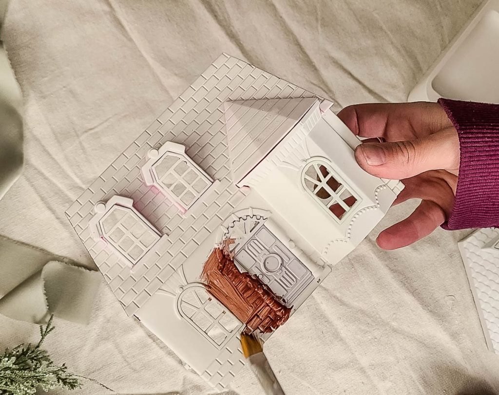 Dollhouse coated in white primer, transitioning to a warm touch with brown acrylic paint in progress for a charming DIY gingerbread house project