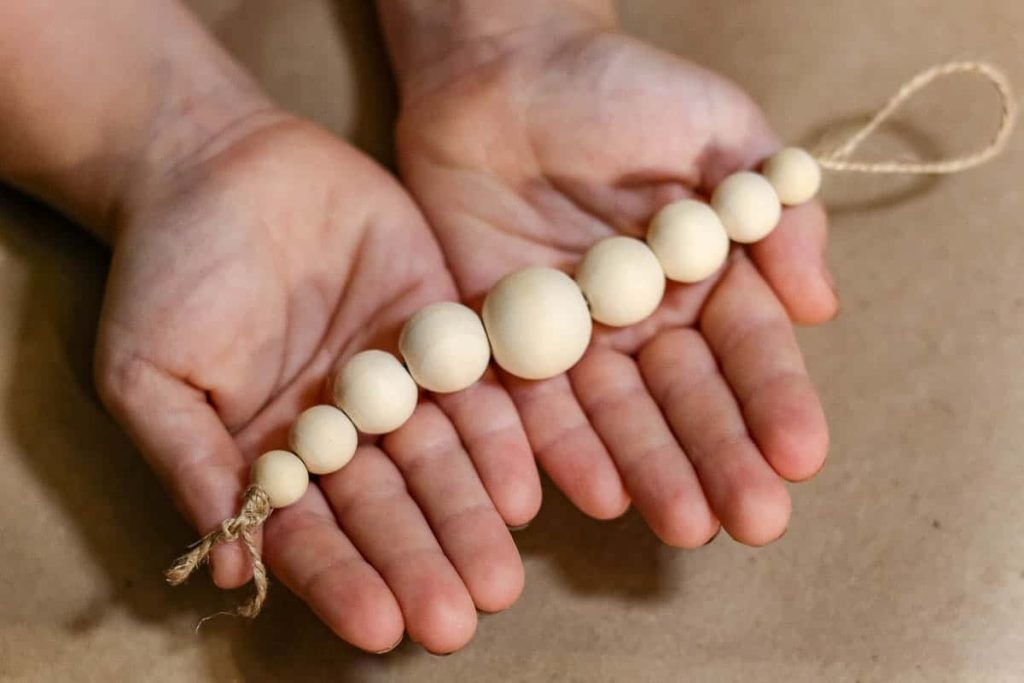 A person is holding a length of twine, to which beads are attached.