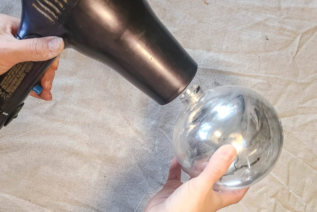 The person holds the dryer to speed up the process of drying and make it more efficient while holding the ornaments.