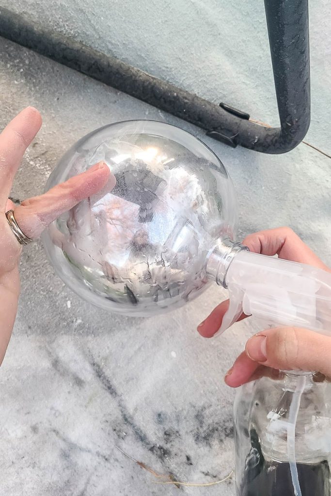 The person sprays vinegar into a mercury glass ornament.