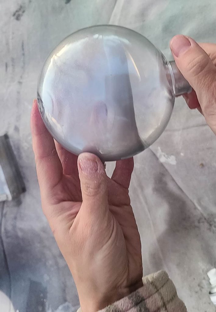 The person holds the ornament and rolls the paint onto it.