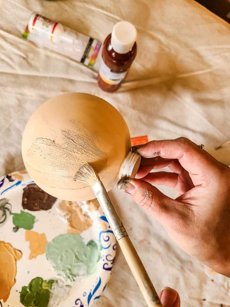 A person is holding a Christmas ball, brushing the mixture of baking soda and paint onto it to create an ornament.