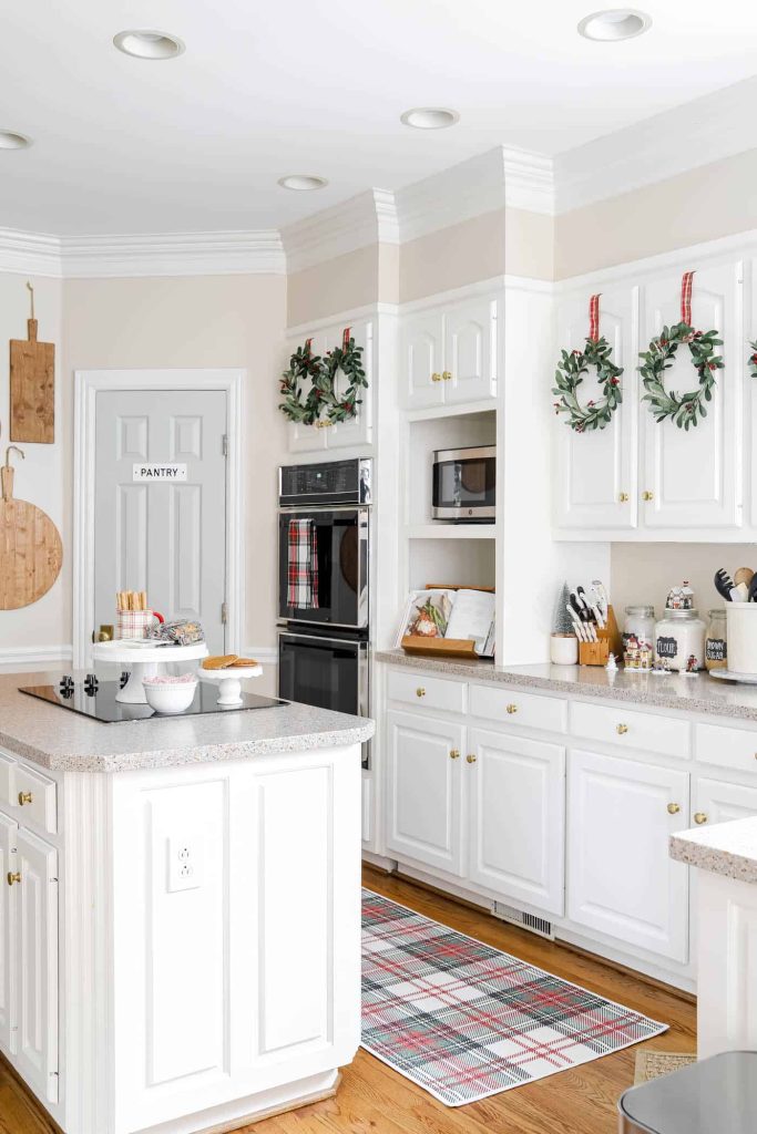 A white kitchen decorated with mini Christmas wreaths hangs on cabinets.