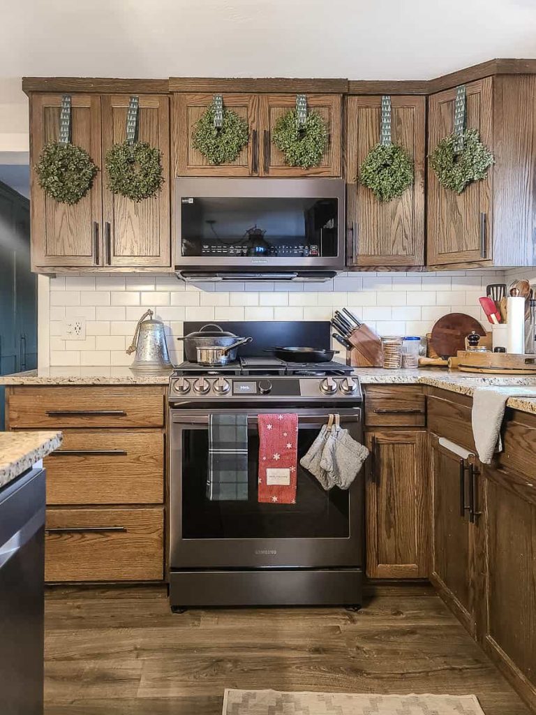 A photo of a mini wreath hangs on kitchen cabinets for Christmas.