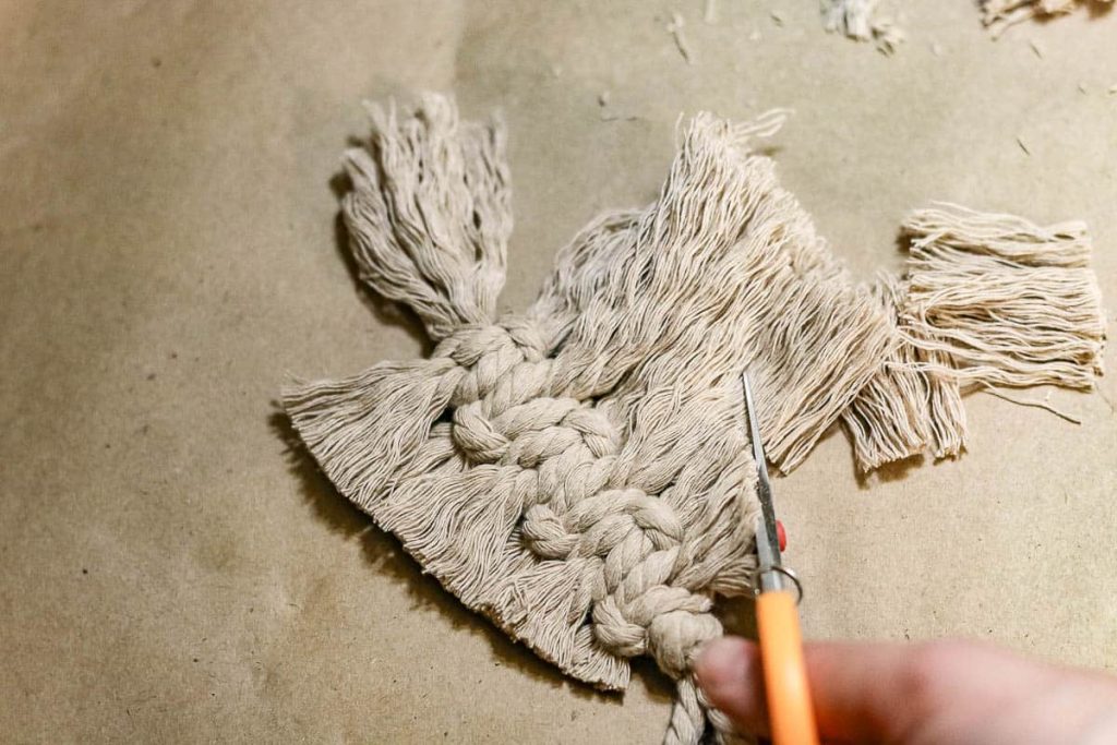 A photo of a person trimming the branches on a Macrame Christmas tree using scissors