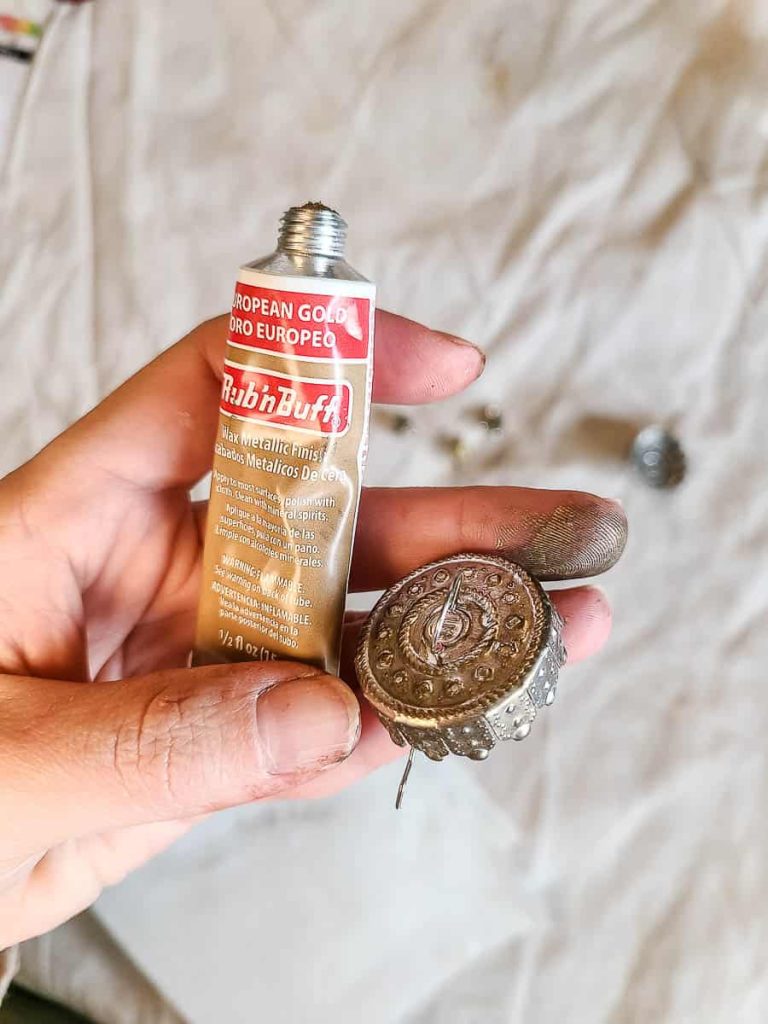 A person rubs Rub 'n Buff onto the metal tops of ornaments.