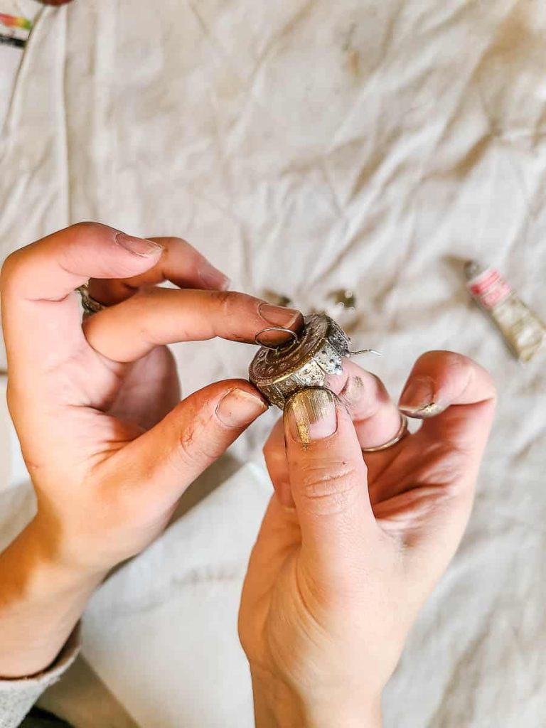 An additional photo shows a person rubbing Rub 'n Buff onto the metal tops of ornaments.