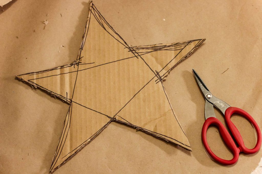 A star drawn on cardboard has already been cut with scissors on the side.