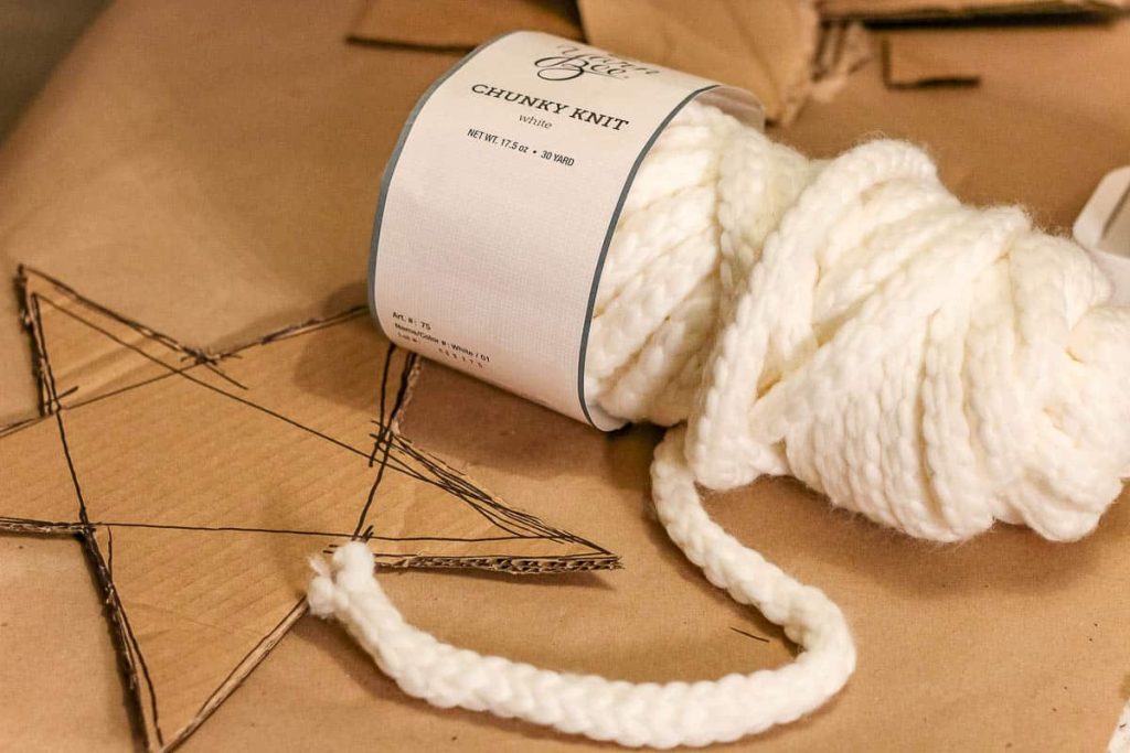 A cut star is drawn on cardboard with a white yarn on the side. On How to make a Christmas tree star topper. 