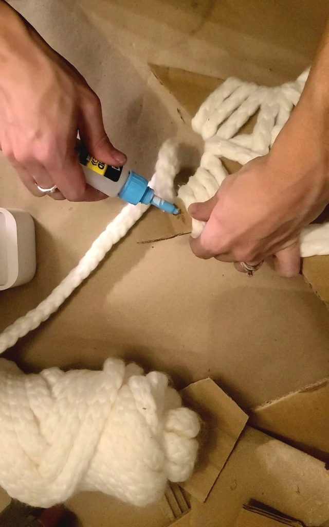 A person is gluing yarn to a star-shaped cardboard.