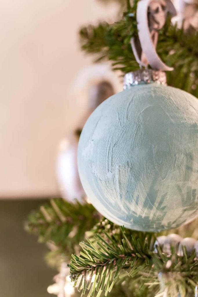 A detailed view of a sophisticated gray Christmas ball ornament elegantly nestled within the branches of a Christmas tree, adding a touch of modern and refined charm to the festive decor.