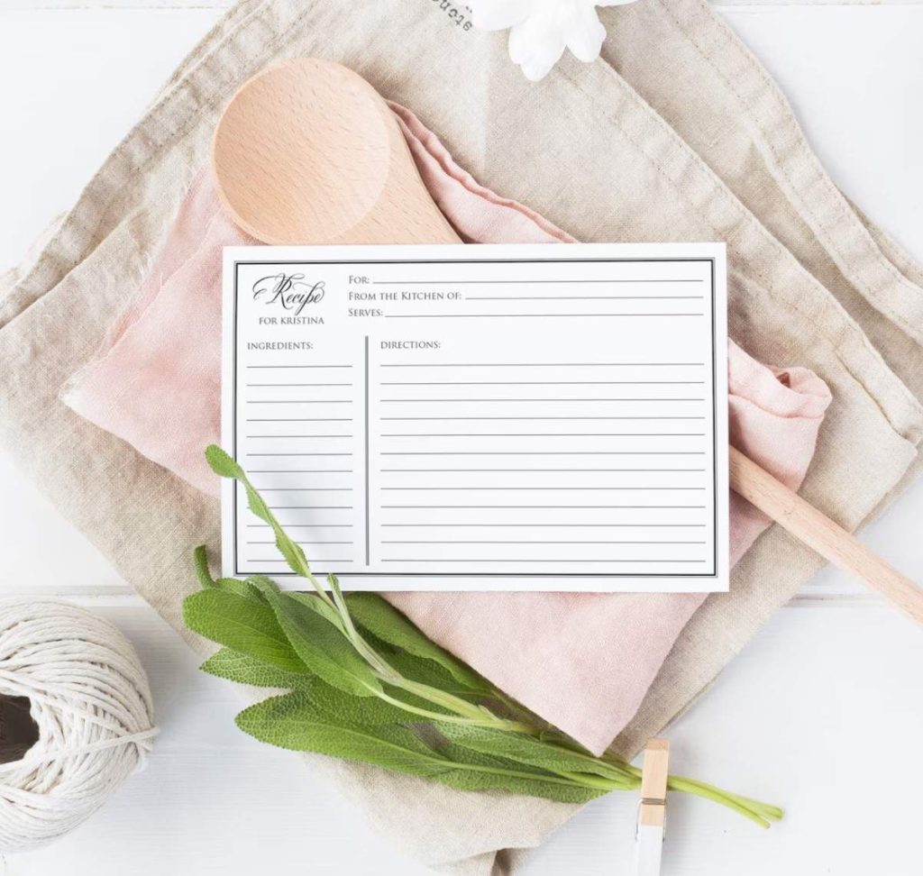Pretty recipe card that is blank and ready to fill in laying on top of linen tea towels, a wooden spoon and some kitchen twine 
