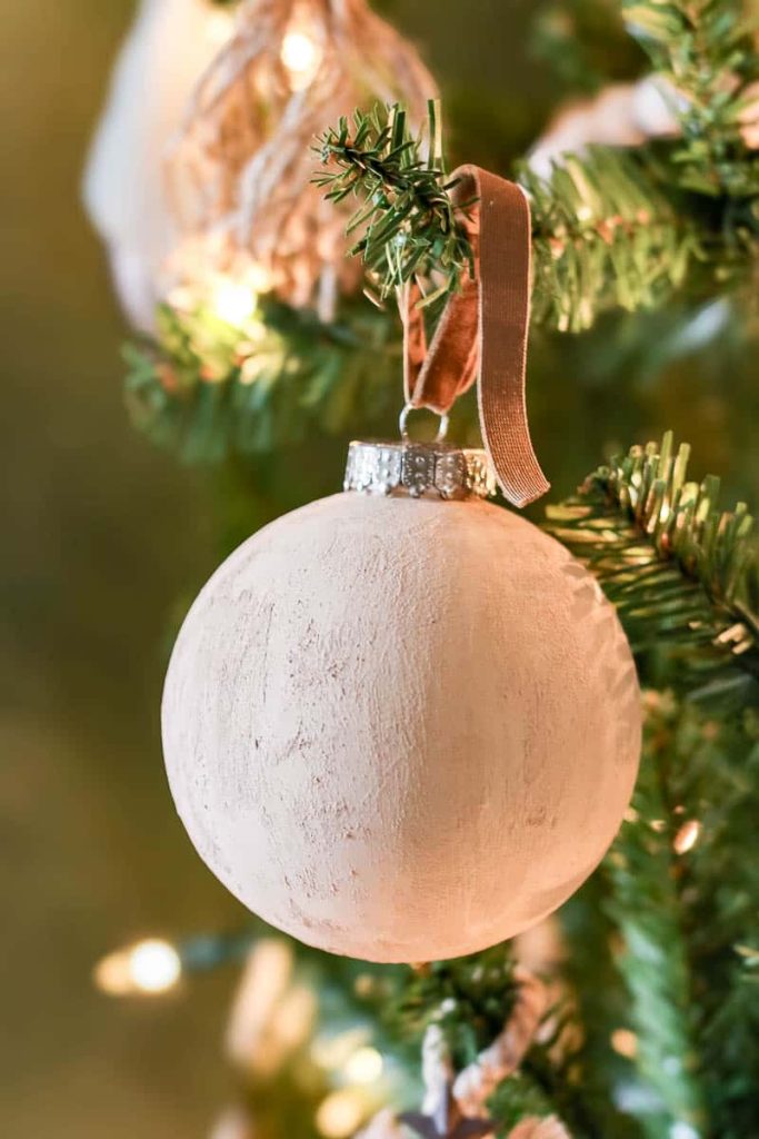 A close-up view of a delicate beige Christmas ball ornament, gracefully hanging amidst the branches of a Christmas tree, adding subtle warmth and elegance to the festive holiday display