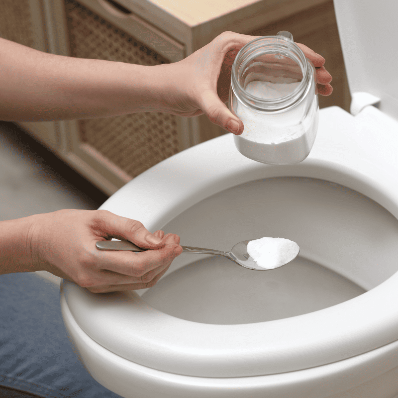 A person is using a baking soda paste to clean the toilet bowl.