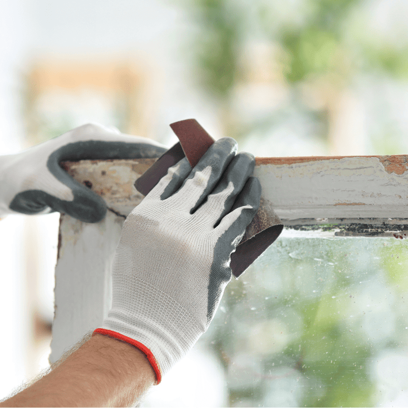 A man uses sandpaper to smooth the surface of an old window.