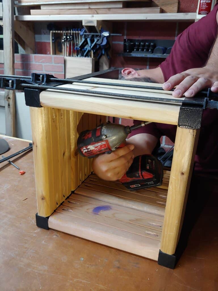 A man is assembling the sides to connect them to the legs, forming a box for a planter. 