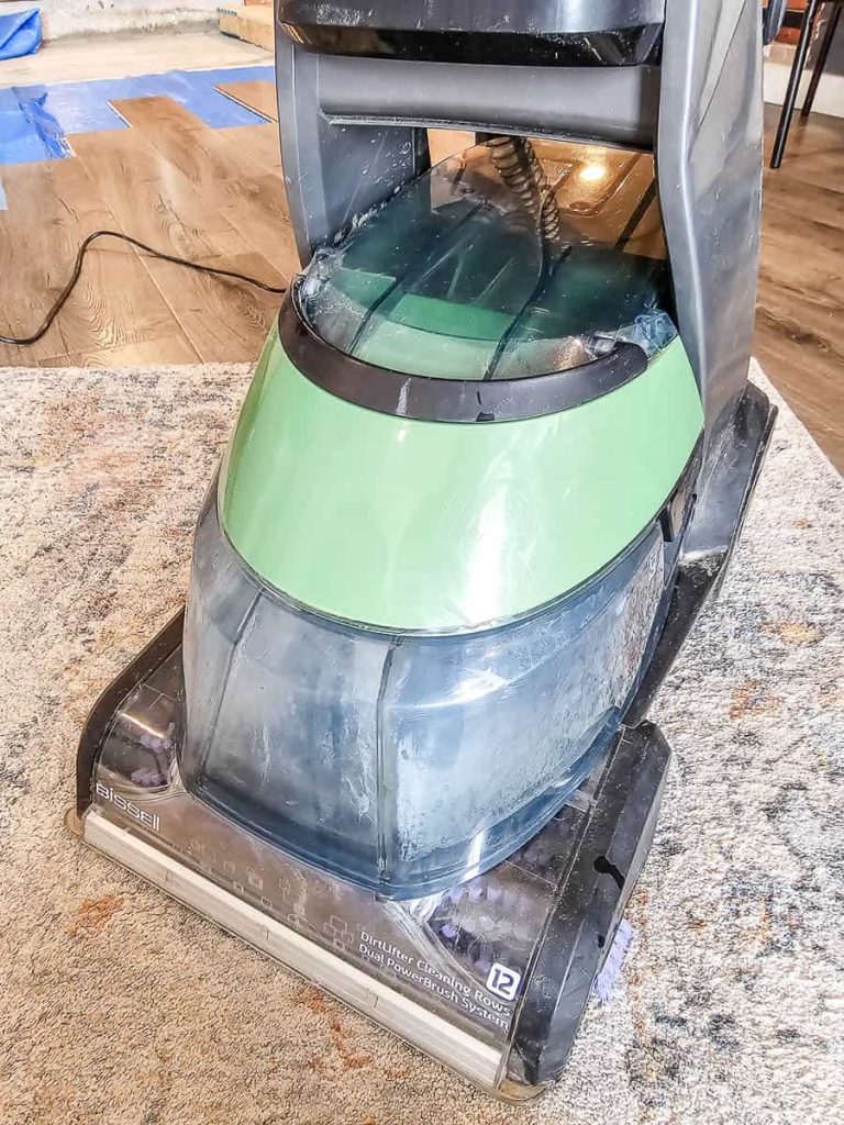 The photo shows someone using a rug shampooer to clean an area rug.