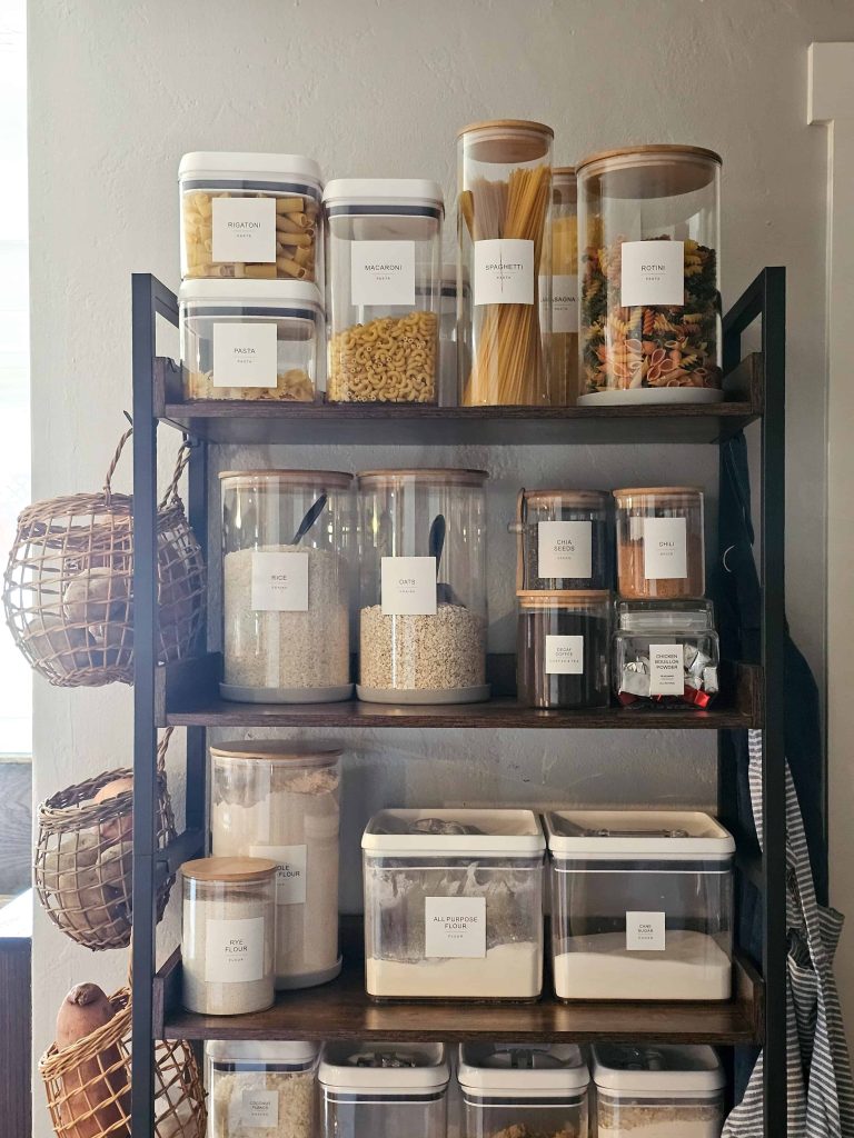 A well-organized kitchen pantry featuring neatly arranged food containers on shelves, accompanied by a basket placed on the side.