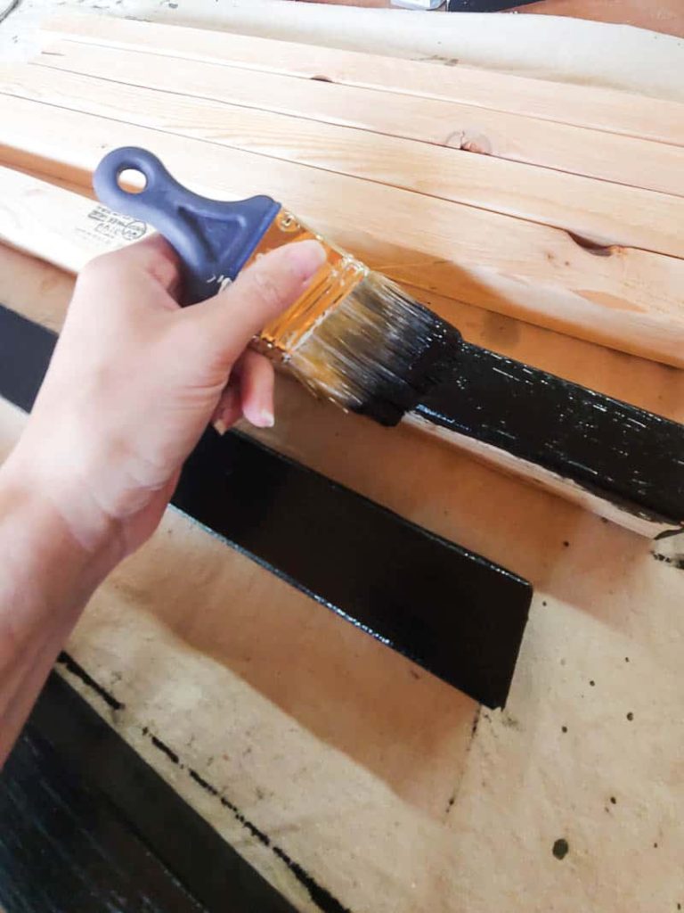 An individual is applying paint to the leg and top pieces of a modern planter box.