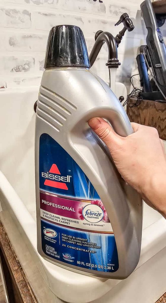 A woman is holding a bottle of carpet cleaner freshener in the photo.


