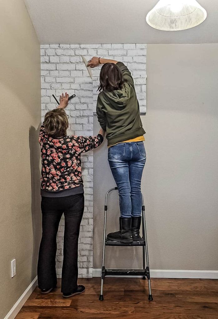 Continue the process as a person uses a squeegee to press the wallpaper onto the wall, ensuring a smooth surface and working out any bubbles along the way.