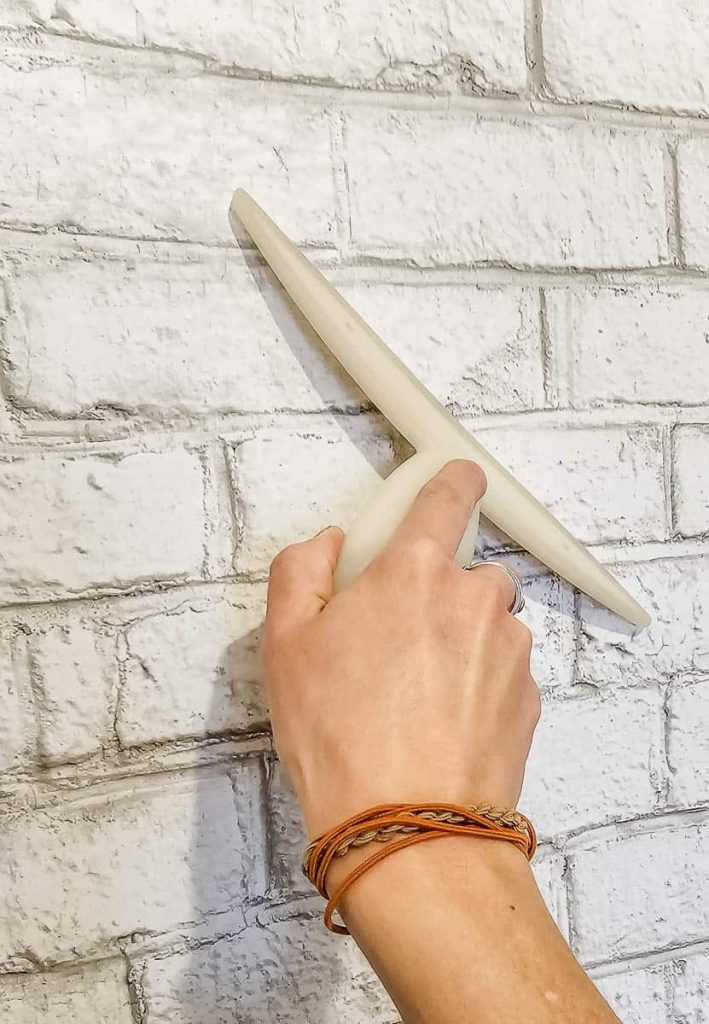 The process of using a squeegee to press the wallpaper onto the wall, ensuring a smooth application and working out any bubbles along the way.