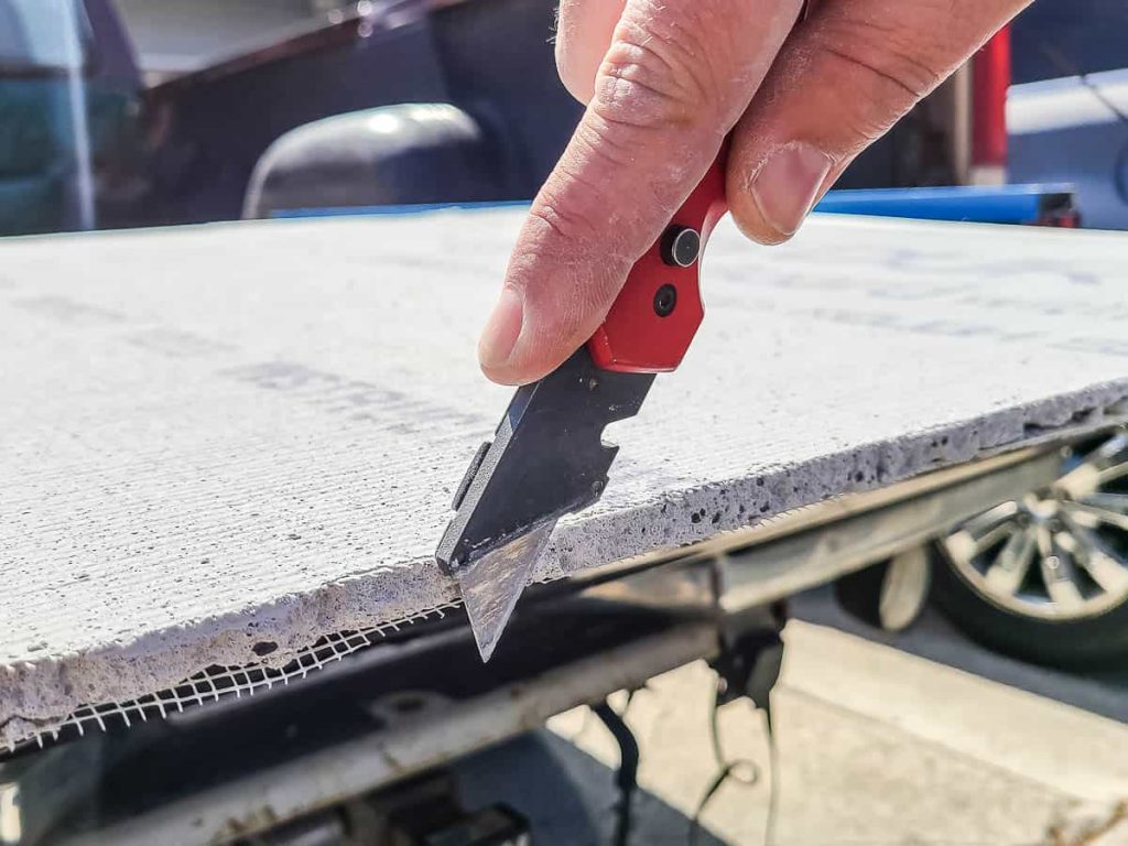A utility knife is being used to cleanly cut the edge of the cement board.