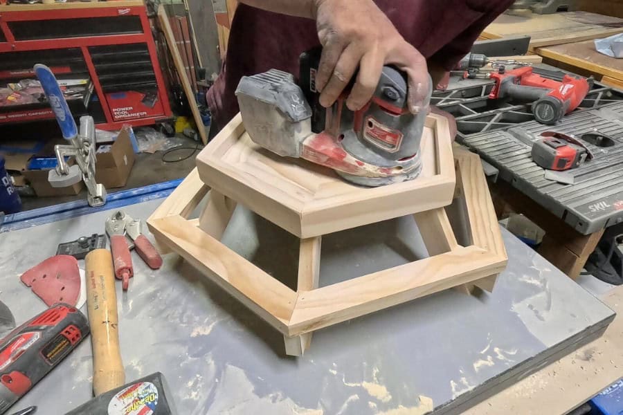 The man is sanding the Chicknic Table again for a smooth finish.