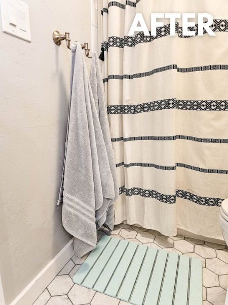 Bathroom showing two gold towel hooks on wall with two gray towels and bath mat in front of shower made from natural mineral diatomite 