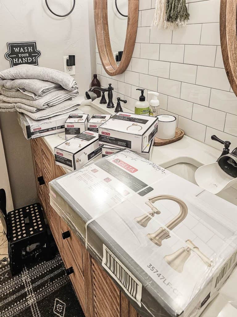 Bathroom with boxes of new faucets and accessories on countertop from Delta with a stack of new gray towels