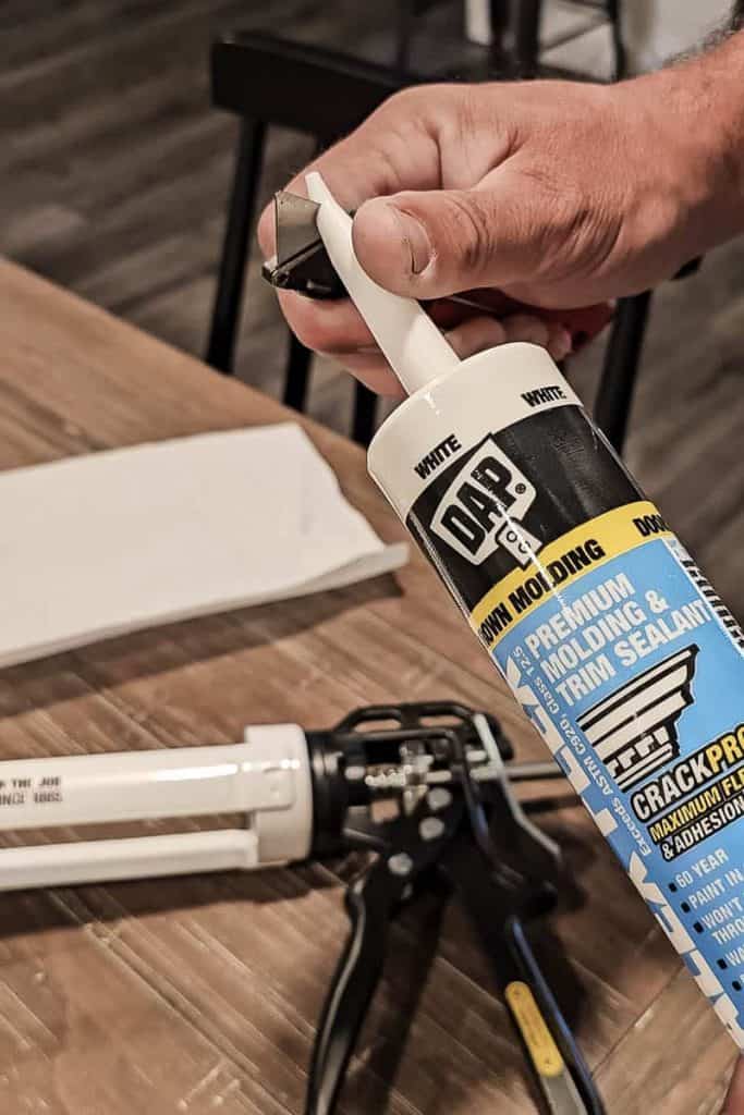 A photo of a man opening a tube of DAP Alex Flex caulk, preparing to apply it for a home improvement project.