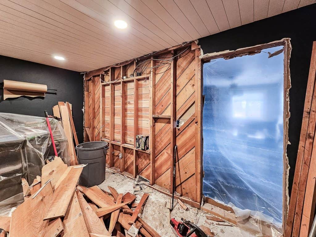 Process shot of removing interior wall with one side of drywall and paneling removed to reveal interior studs and electrical