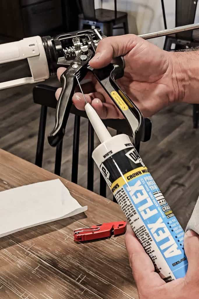 A photo of a man loading DAP Alex Flex caulk into a caulking gun, ready to apply it for a home repair or renovation project.