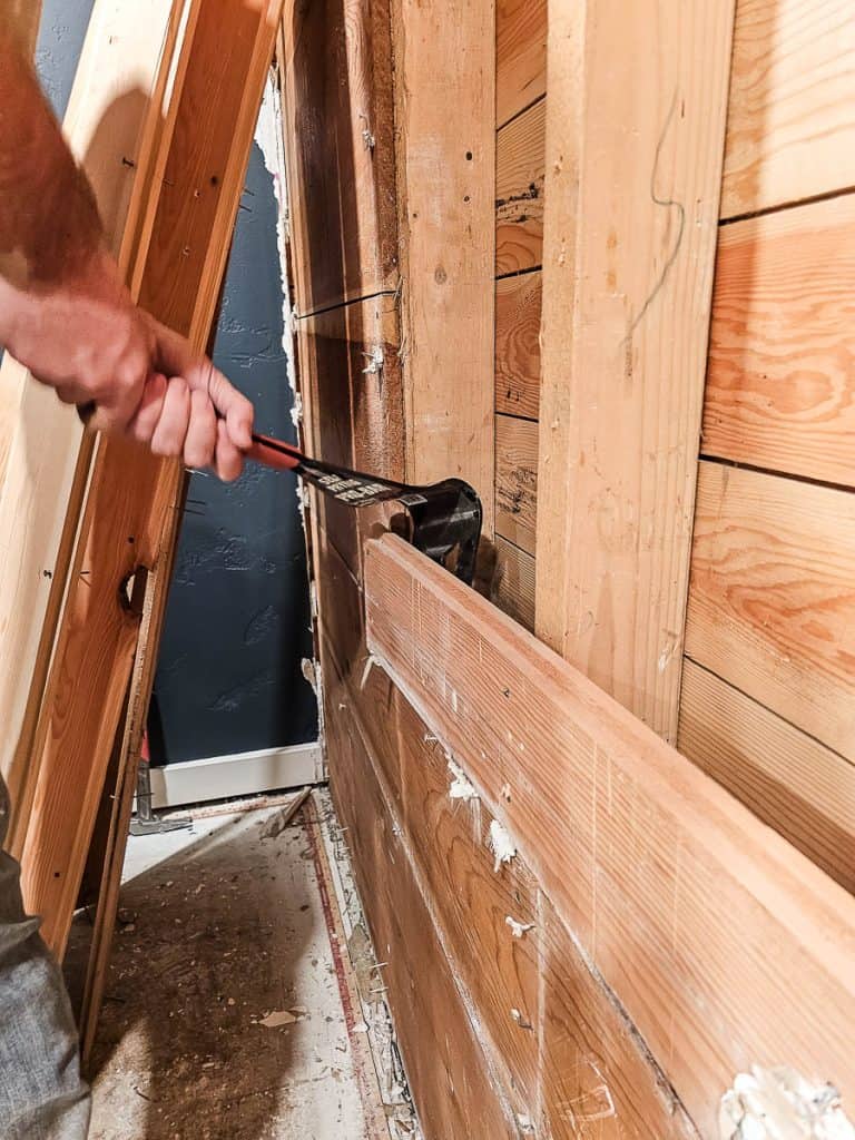 Pulling back old wood paneling on interior walls with pry bar during renovation