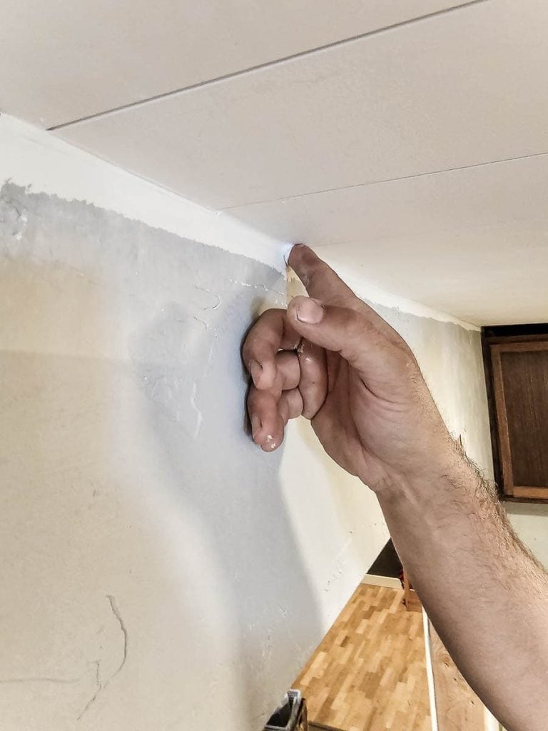 A photo of a man using his finger or a caulk finishing tool to smooth and shape the applied DAP Alex Flex caulk along the ceiling for a seamless finish.