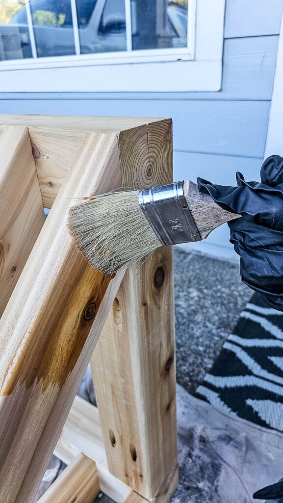 A photo of a wooden bike rack with a man using a paintbrush to stain the wood.